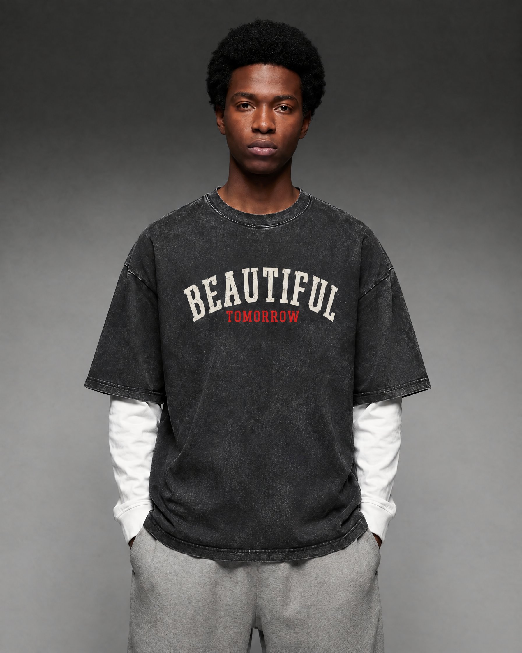 Model in the washed black Varsity Tee with red TOMORROW lettering, layered over a white long sleeve, with grey sweatpants